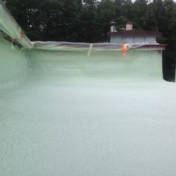 Techniczne Usługi Natryskowe - Świeżo nałożona, jasna pianka PUR na płaskiej powierzchni dachu, zabezpieczona folią i taśmą malarską przy krawędziach. Widoczne drzewa w tle.