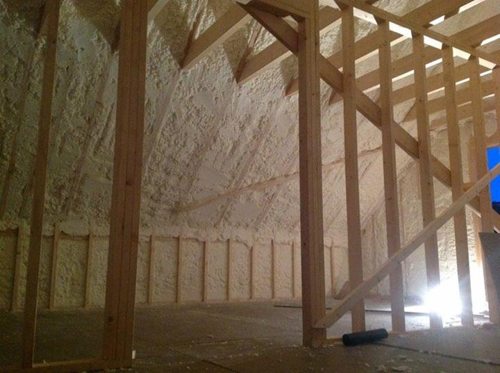 Poddasze po ociepleniu pianką PUR, widoczne drewniane elementy konstrukcji i jasna, nierówna powierzchnia izolacji natryskowej na ścianach i dachu.