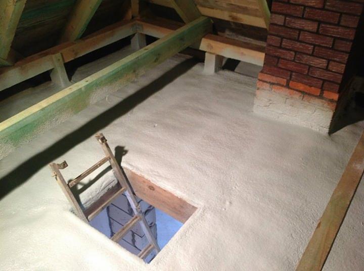 Poddasze po ociepleniu pianką PUR: drewniana konstrukcja, ceglany komin, drabina w otworze. Widok z góry ukazuje równomierną warstwę izolacji.