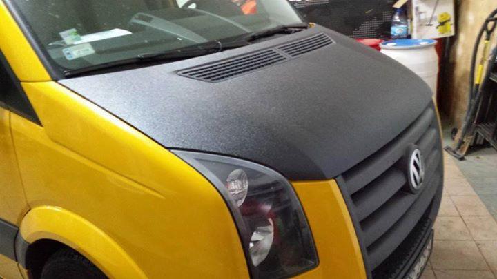Żółty van Volkswagen Crafter z matową, grafitową folią na masce, widok z przodu, z detalami grilla i reflektorów. Nietypowe wykończenie maski.