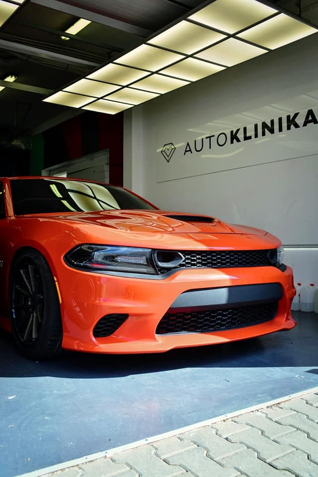Pomarańczowy Dodge Charger po zabiegach w autoklinice, widoczne logo firmy na ścianie, czyste i lśniące nadwozie.