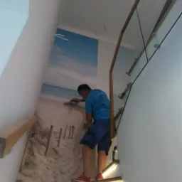 Pracownik wygładza tapetę z motywem plaży na ścianie klatki schodowej z podświetlanymi stopniami i szklaną balustradą.