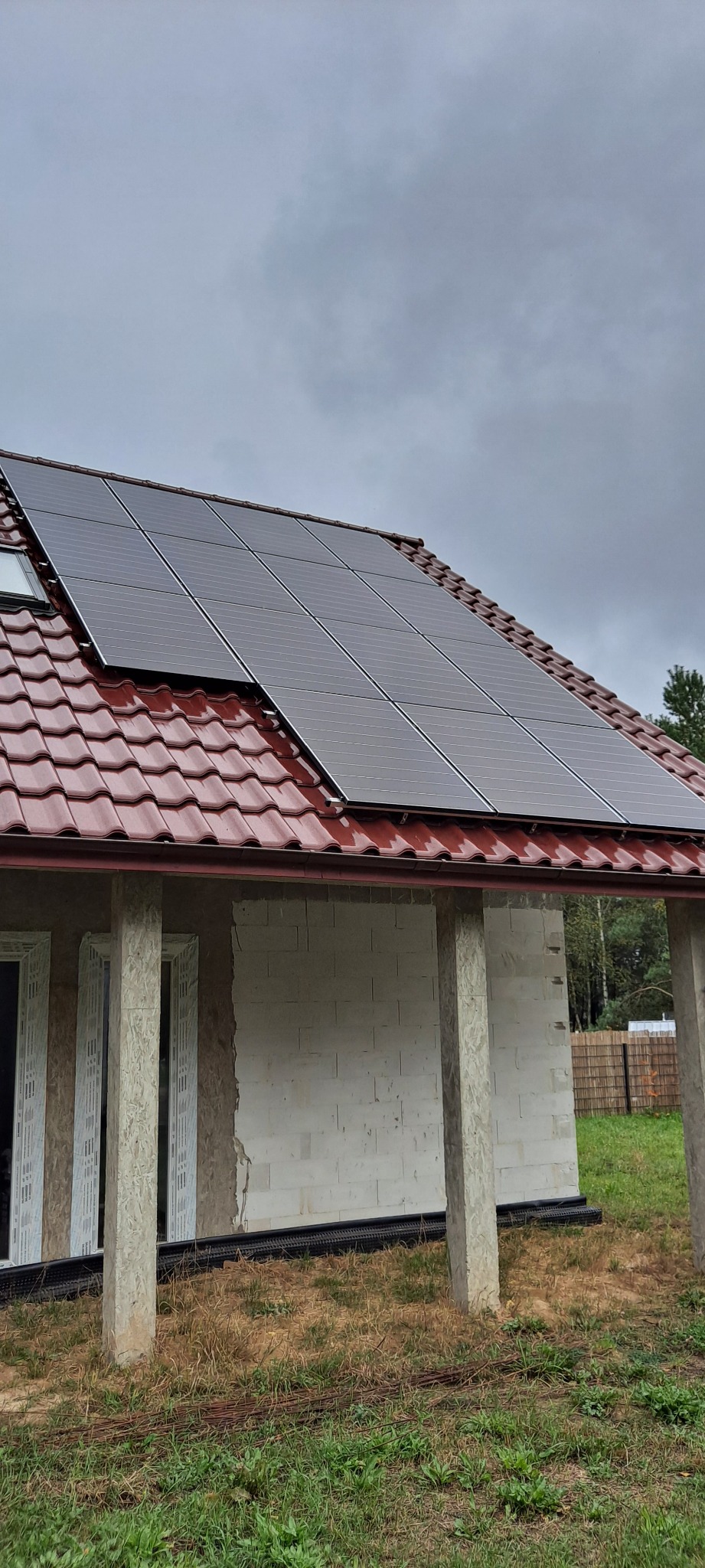 Panele słoneczne na czerwonym dachu domu w trakcie budowy w Pile, widoczne szare niebo.