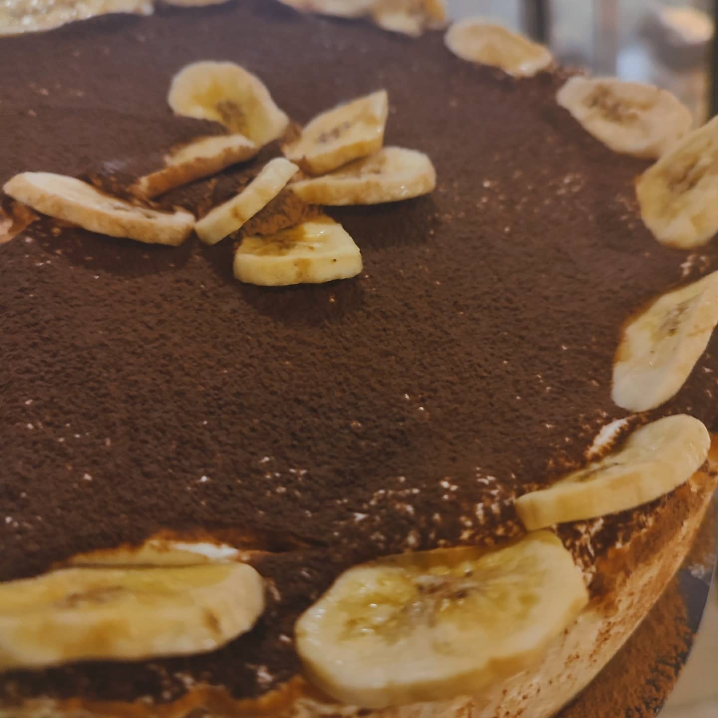 Tort czekoladowy z kremem i dekoracją z plasterków banana, posypany kakao.