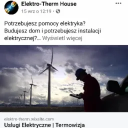 Elektryk w kasku, stojący obok samochodu, sprawdza dane na tablecie na tle farmy wiatrowej i pochmurnego nieba.