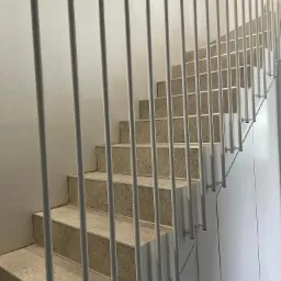 Nowoczesne schody z terazzo z minimalistyczną balustradą z pionowych, białych rurek, mocowanych do ściany.