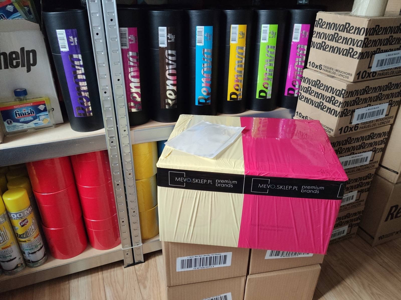 Półka magazynowa z zapasem produktów: kolorowe opakowania papieru toaletowego Renova w tubach, pudełka chusteczek higienicznych, środki do czyszczenia w sprayu oraz płyn do mycia naczyń Finish,...