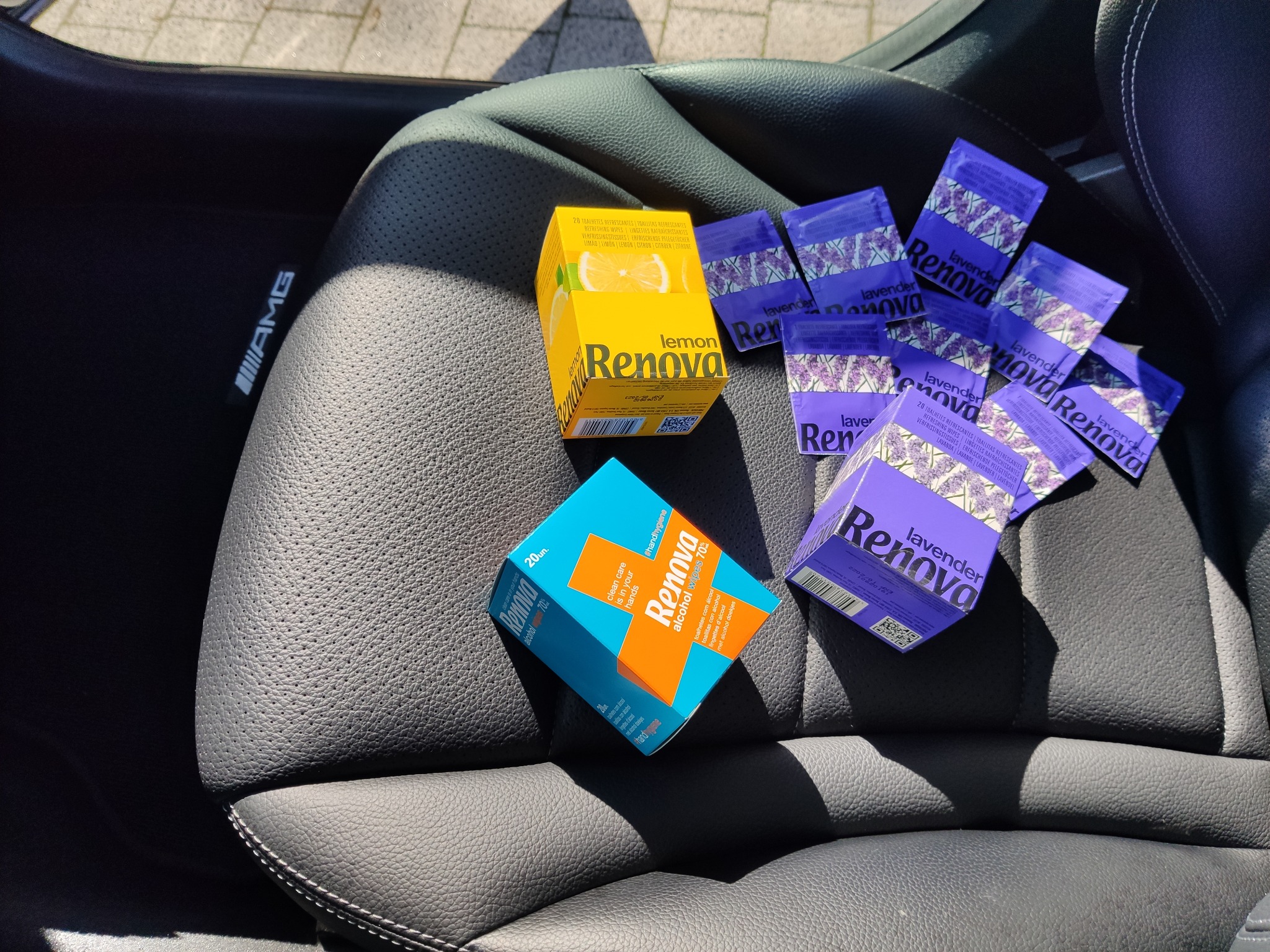 Pudełka i saszetki nawilżanych chusteczek Renova o zapachach cytrynowym i lawendowym leżące na czarnym, skórzanym fotelu samochodowym marki AMG.