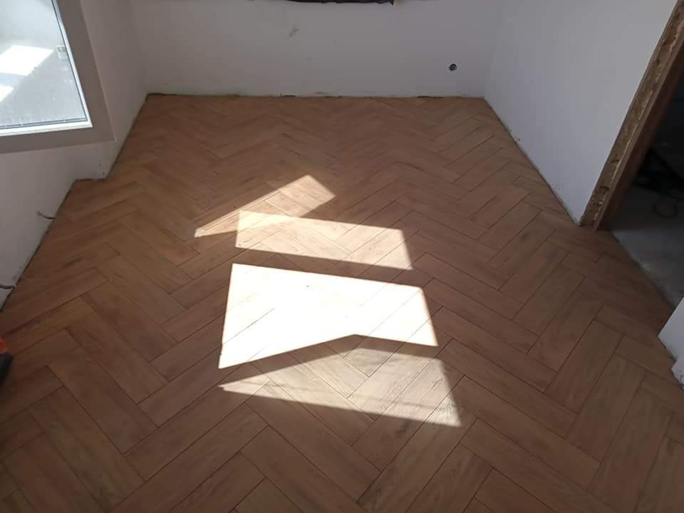 Ułożona drewniana podłoga w jodełkę w pokoju, widoczne promienie słoneczne padające na parkiet.