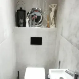 Mała toaleta z umywalką i półką z dekoracjami, szare płytki imitujące kamień na ścianach.