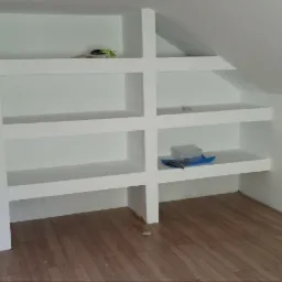 Półki z płyty karton gips wnękowe w skosie poddasza, z widocznymi narzędziami i pojemnikiem na śruby na jednej z półek, podłoga wyłożona panelami.