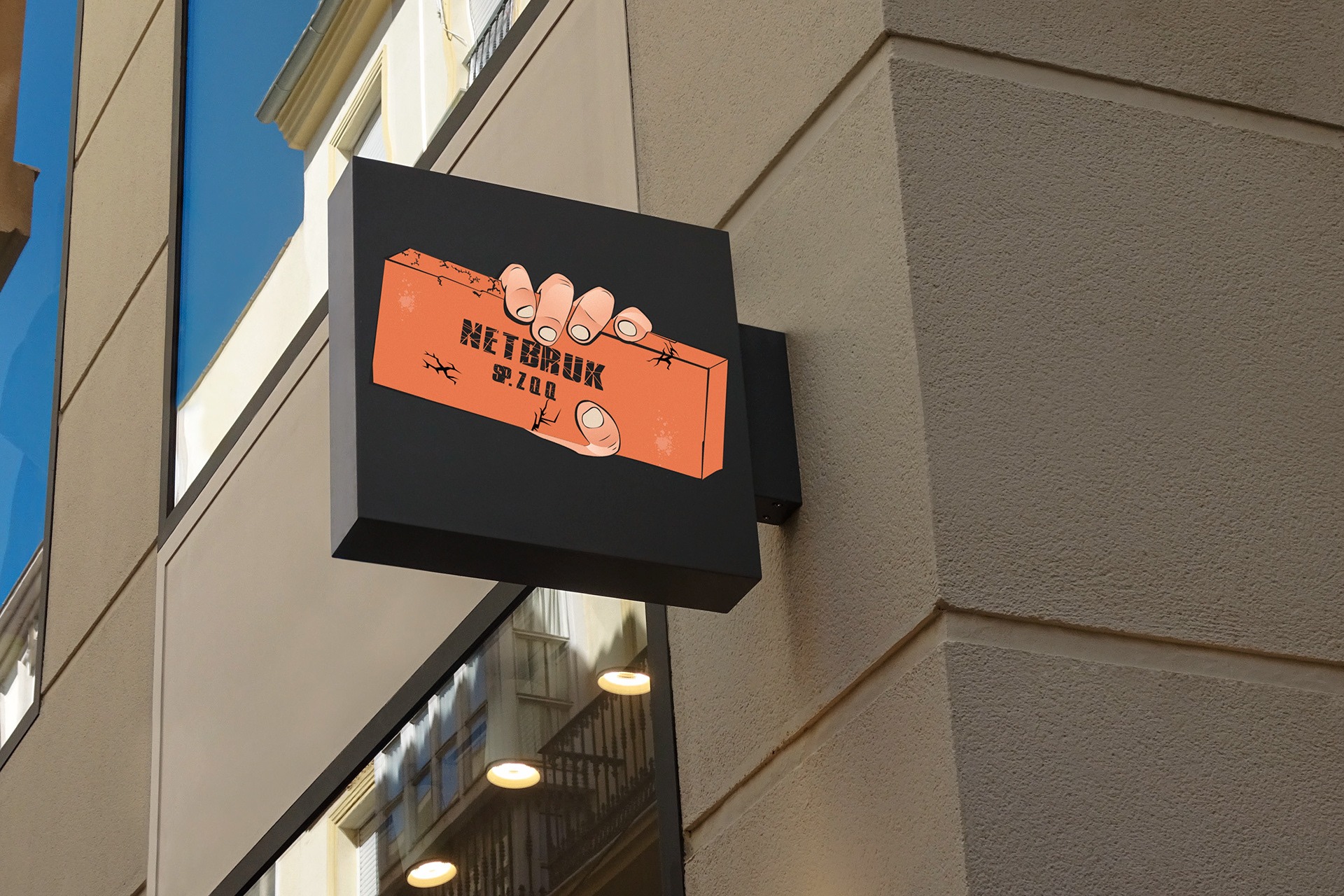 Czarny szyld reklamowy na ścianie budynku z grafiką dłoni trzymającej cegłę z napisem 'NETBRUK SP. Z O.O.'.