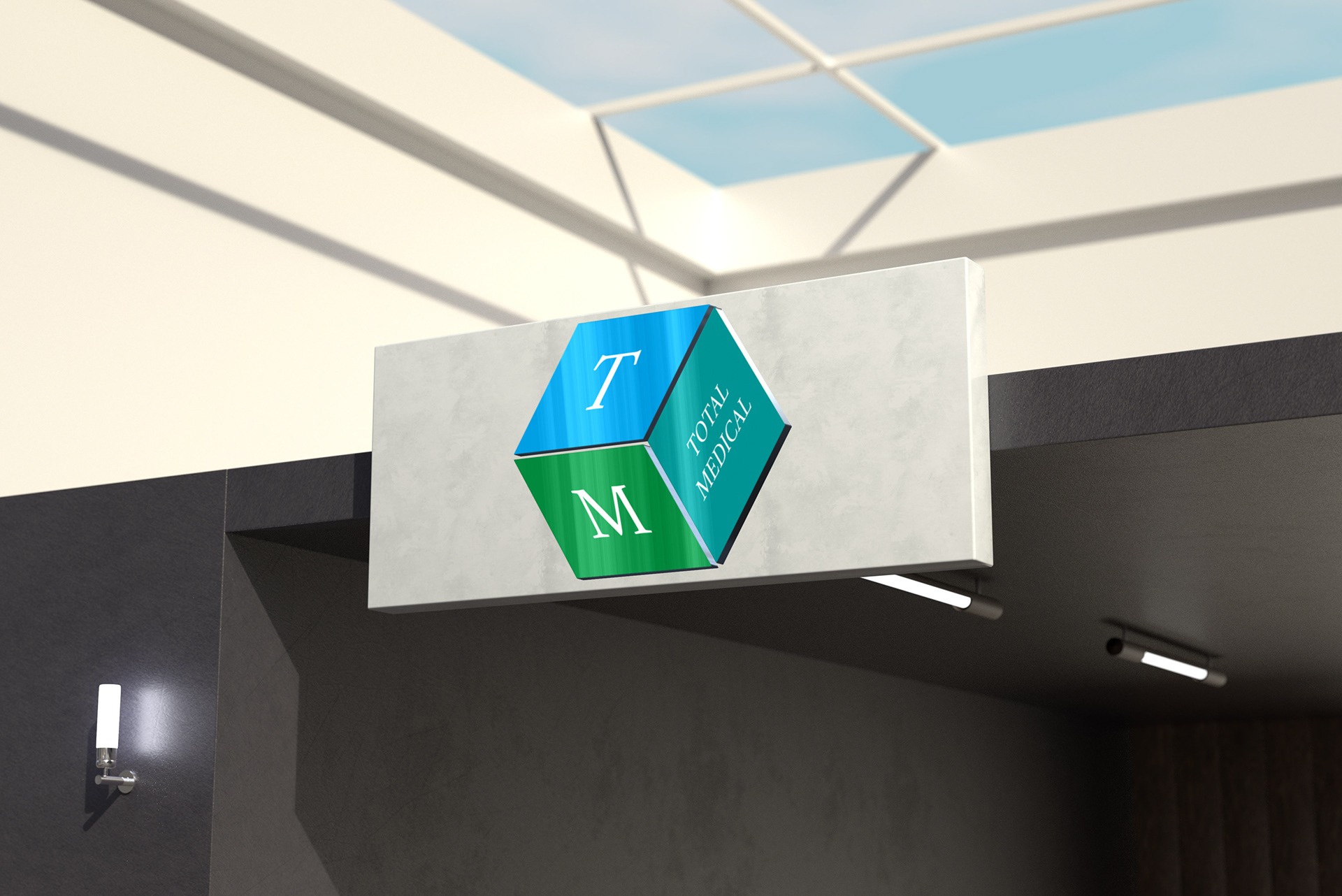 Szyld reklamowy w formie kostki z literami T i M w kolorach niebieskim i zielonym oraz napisem 'TOTAL MEDICAL', zamocowany pod sufitem w nowoczesnym wnętrzu z oświetleniem punktowym.