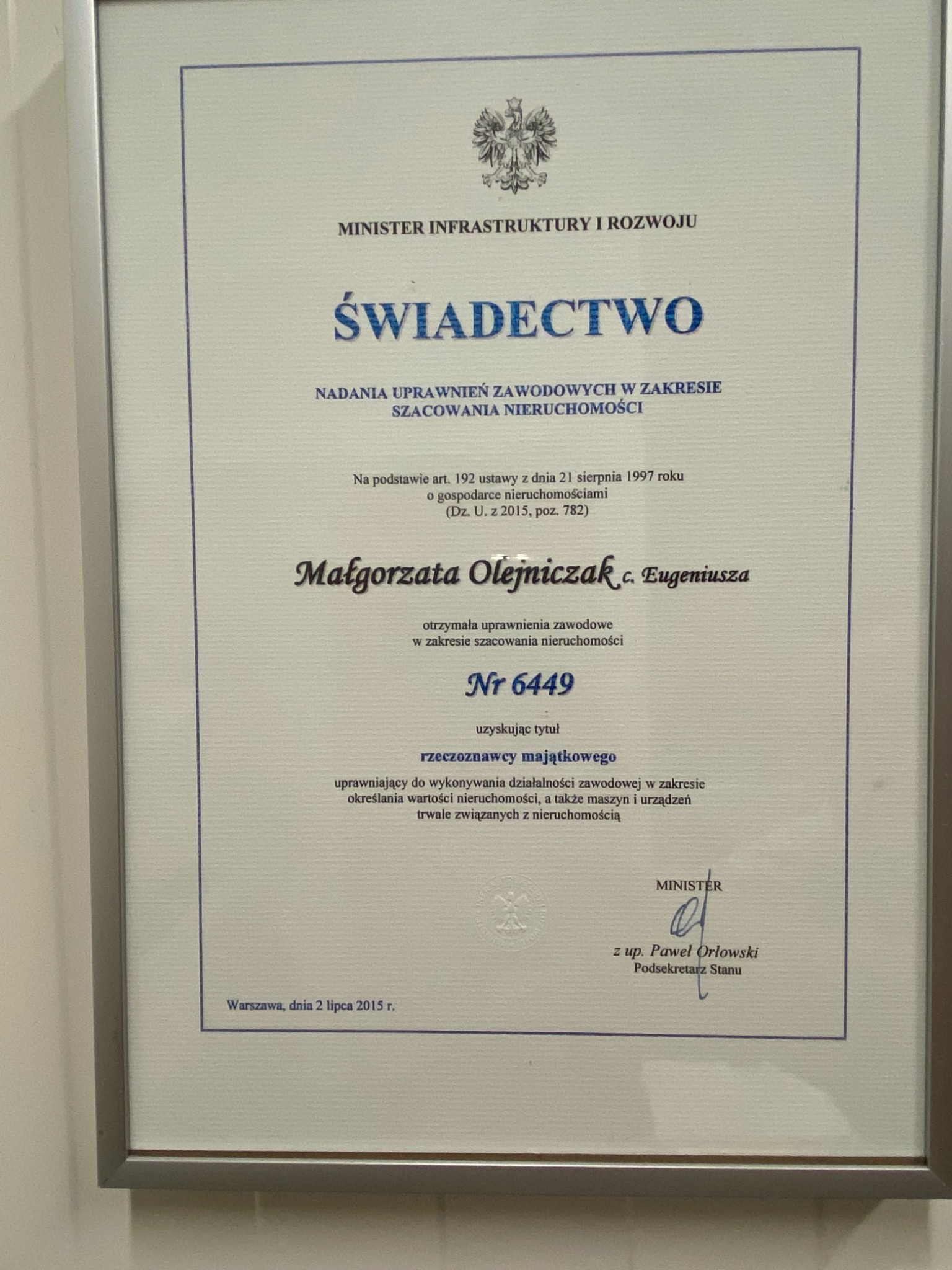 Skan świadectwa nadania uprawnień zawodowych w zakresie szacowania nieruchomości, wydanego przez Ministra Infrastruktury i Rozwoju dla Małgorzaty Olejniczak, oprawionego w ramkę.