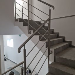 Usługi spawalniczo monterskie - Nowoczesne schody z szarymi płytkami i metalową balustradą. W tle widoczne narzędzia i puszki z farbą, sugerujące prace wykończeniowe w budynku.