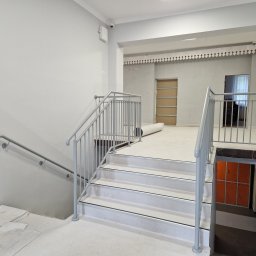 Usługi spawalniczo monterskie - Jasne schody z szarą, metalową balustradą w budynku. Widoczne zabezpieczenia na podłodze i ścianach. Ujęcie z dołu, podkreślające konstrukcję schodów.