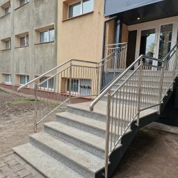 Usługi spawalniczo monterskie - Zewnętrzne schody z szarego granitu prowadzące do budynku, zabezpieczone nowoczesną balustradą ze stali nierdzewnej z pionowymi wypełnieniami. Widok z dołu.