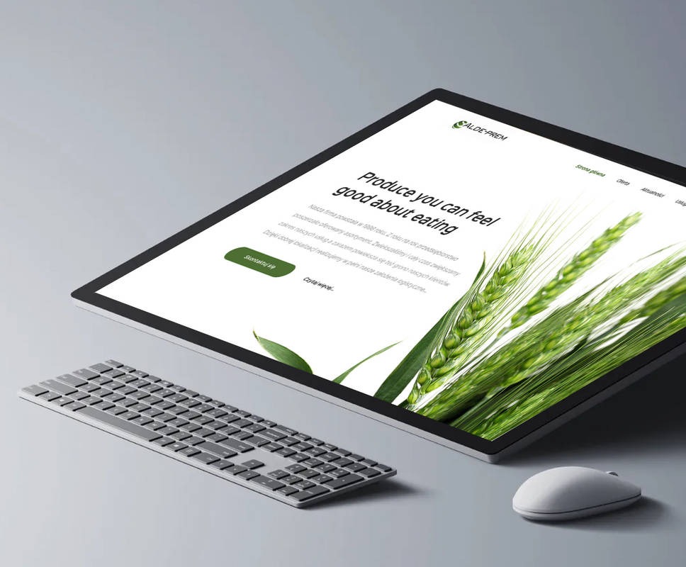 Ekran komputera wyświetlający stronę internetową z zielonym motywem roślinnym, klawiatura i myszka na szarym tle, perspektywa z góry.
