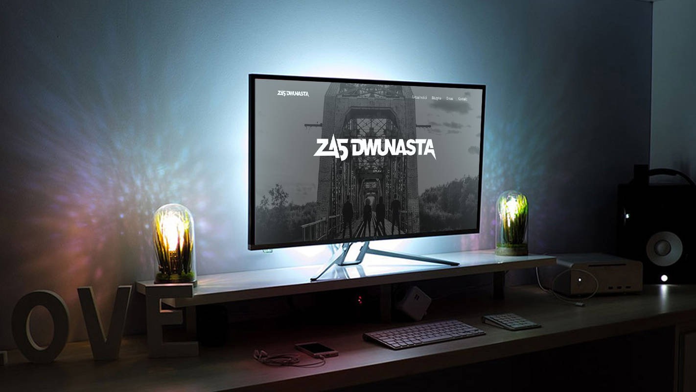 Monitor wyświetla stronę internetową zespołu muzycznego 'Z45 DWUNASTA' z czarno-białym zdjęciem mostu w tle, oświetlony od tyłu diodami LED, na biurku z dekoracyjnymi lampkami i napisem 'LOVE'.