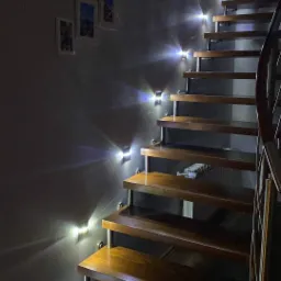 Drewniane schody z podświetleniem LED na ścianie, zdjęcia w ramkach na ścianie, metalowa barierka.