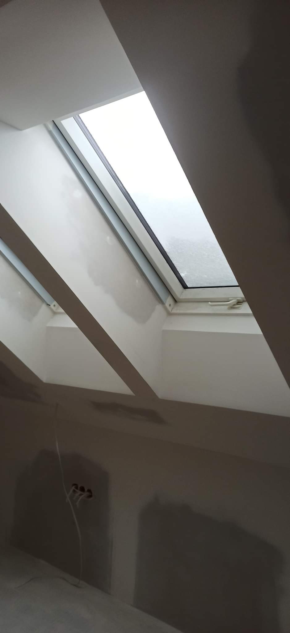 Poddasze z oknem dachowym, wykończone gładzią szpachlową, widoczne wystające przewody elektryczne.