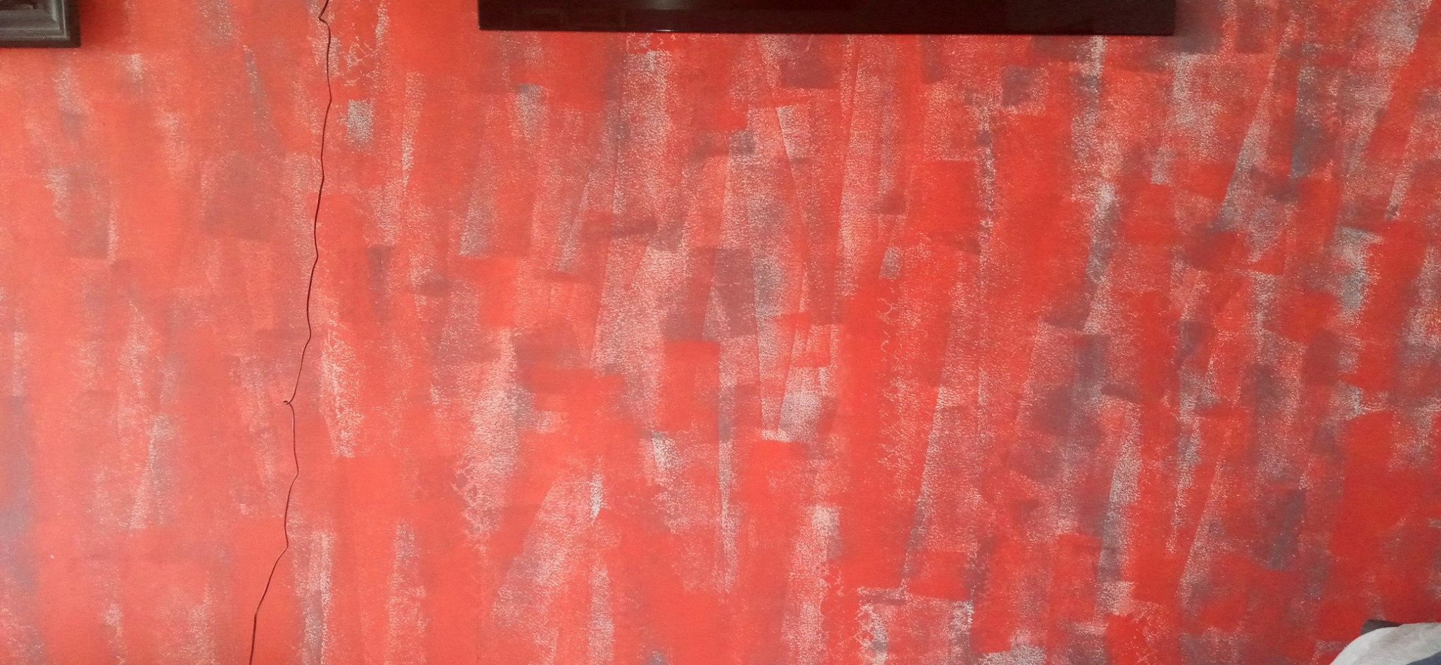 Czerwona ściana z widocznymi pociągnięciami pędzla i szarymi smugami, pionowe pęknięcie na lewej krawędzi ściany, fragment ramy obrazu u góry.