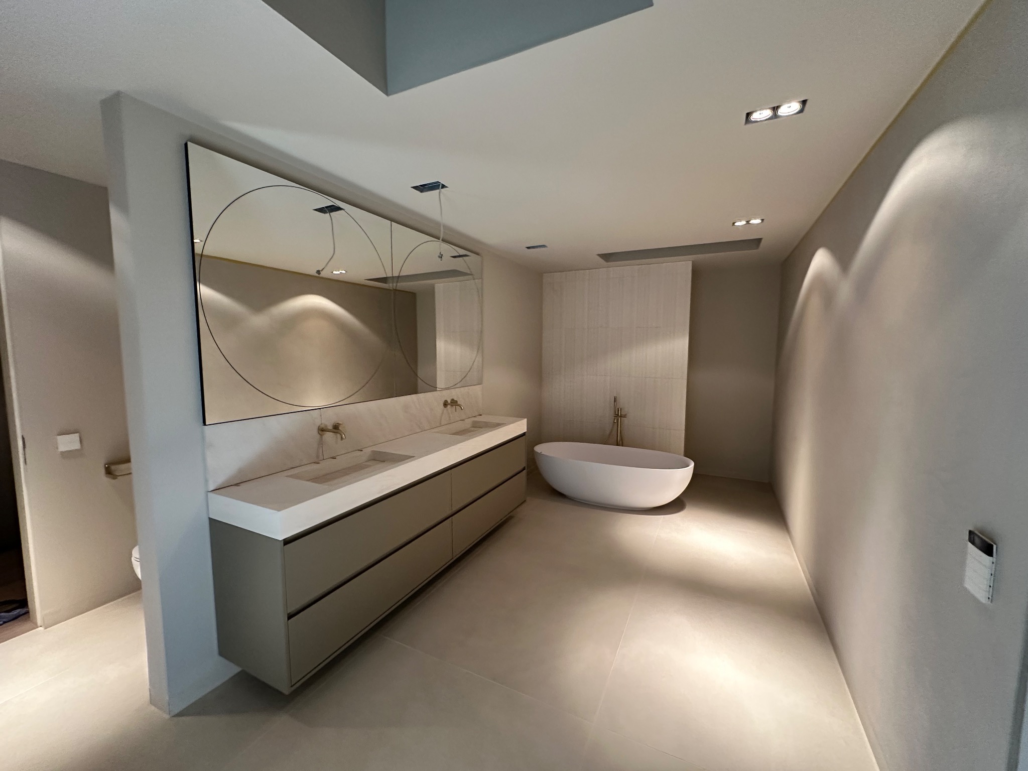 Nowoczesna łazienka z wolnostojącą wanną i podwójną umywalką nablatową z szafkami w odcieniach szarości oraz okrągłymi lustrami podświetlonymi od góry.