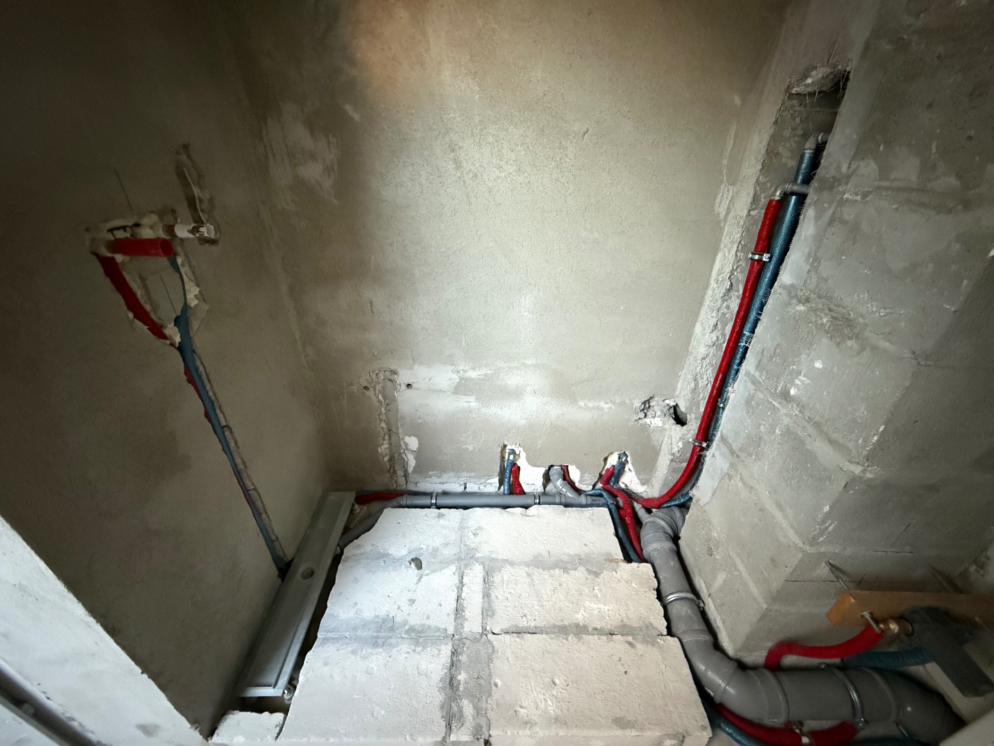 Surowy stan: Instalacja wodno-kanalizacyjna z rurami w kolorze czerwonym i niebieskim, szare rury kanalizacyjne, widoczne ściany w trakcie prac wykończeniowych.