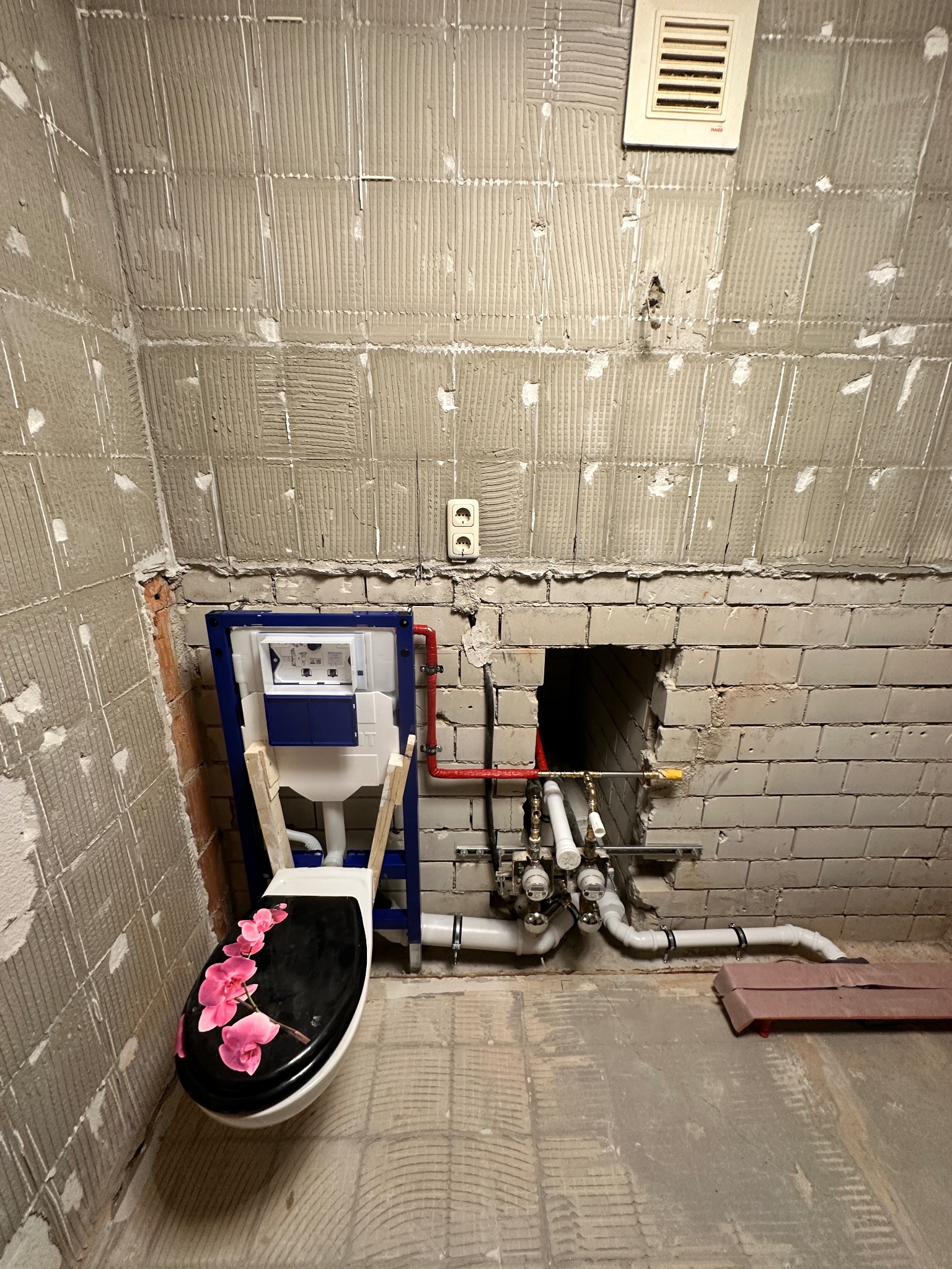 Montaż stelaża podtynkowego WC z dekoracyjną deską, widoczne rury i instalacja wodna w surowej łazience z przygotowanymi ścianami pod płytki. Etap prac hydraulicznych.