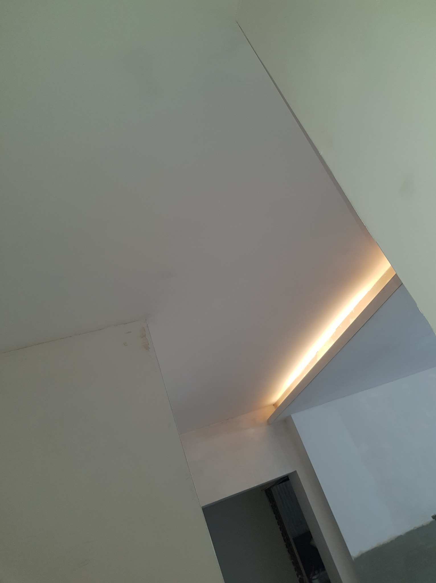 Biały sufit z ukrytym oświetleniem LED, widoczne łączenie płyt gipsowo-kartonowych, fragment drzwi w tle.