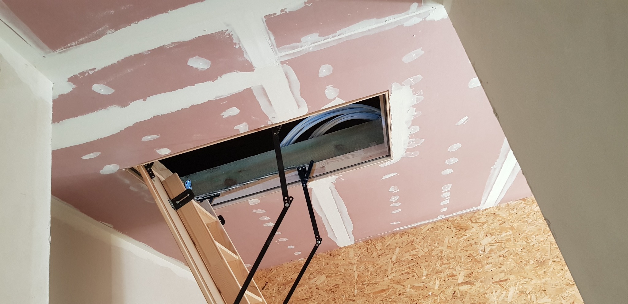 Montaż schodów strychowych z widocznymi przewodami w otworze, płyty gipsowo-kartonowe szpachlowane, ściana z płyty OSB.