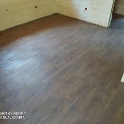 Ukończona podłoga z paneli imitujących drewno w jasnym pomieszczeniu wykończonym boazerią, widoczne otwory na gniazdka elektryczne w ścianie.