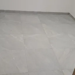 Wykończona podłoga w pomieszczeniu z szarych, kwadratowych płytek imitujących kamień, widok przez otwarte drzwi z drewnianą ościeżnicą.