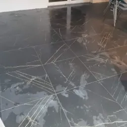 Połyskująca, czarna podłoga z płytek imitujących marmur z wyraźnymi złotymi żyłami, odbijająca światło, z widocznymi krzesłami w tle.