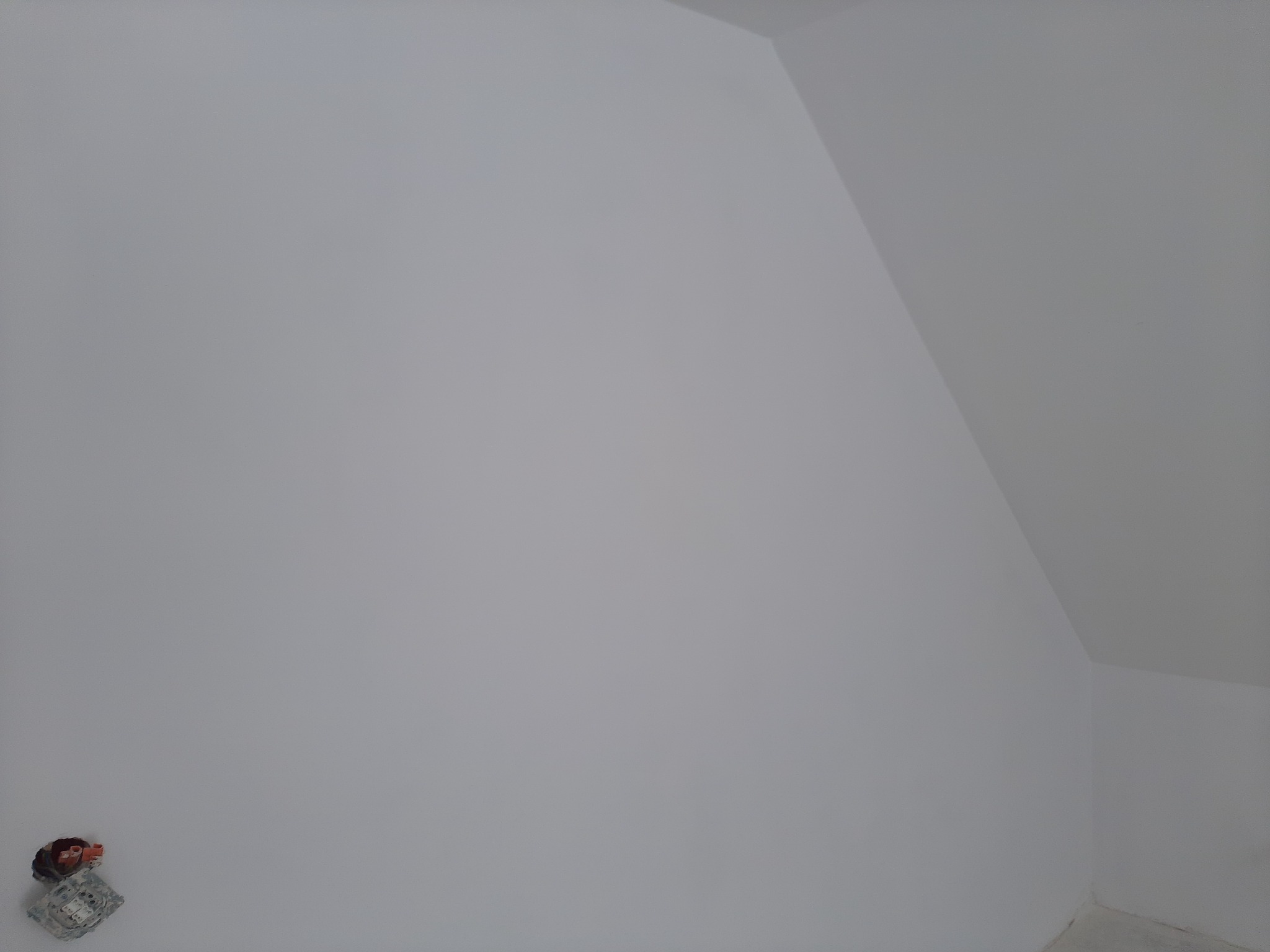 Świeżo pomalowana na biało ściana pod skosem na poddaszu z widocznym gniazdkiem elektrycznym w dolnym rogu.