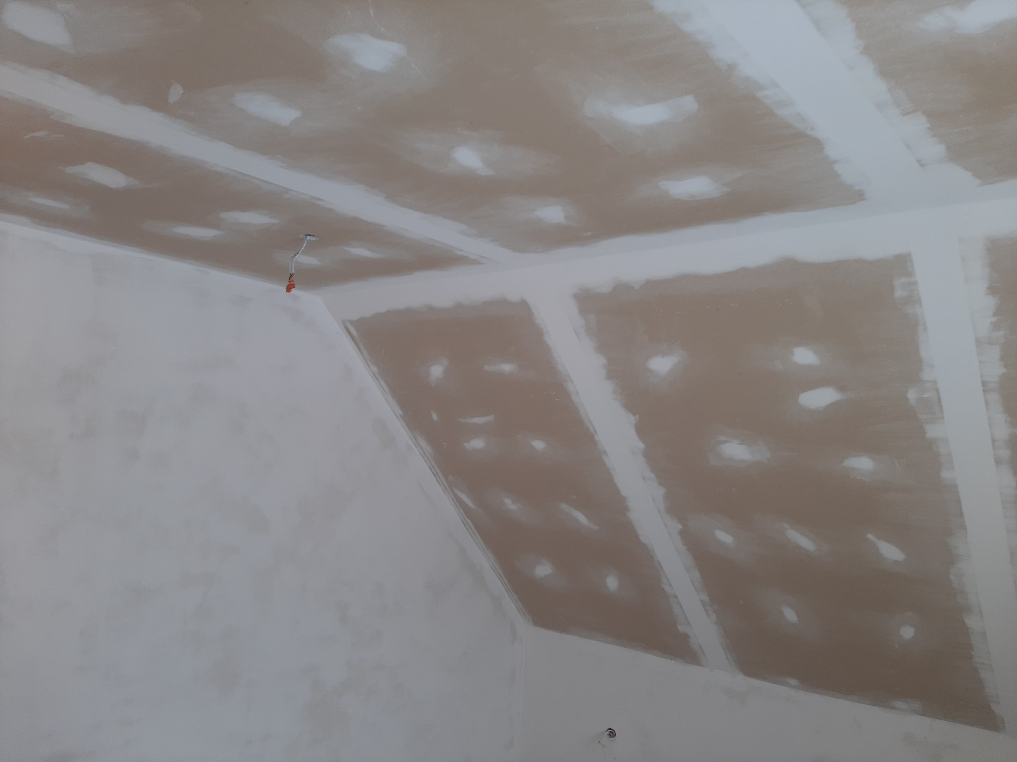 Sufit poddasza z płyt kartonowo-gipsowych, widoczne szpachlowane łączenia i otwory po wkrętach, przygotowany do malowania, z wystającym kablem elektrycznym.