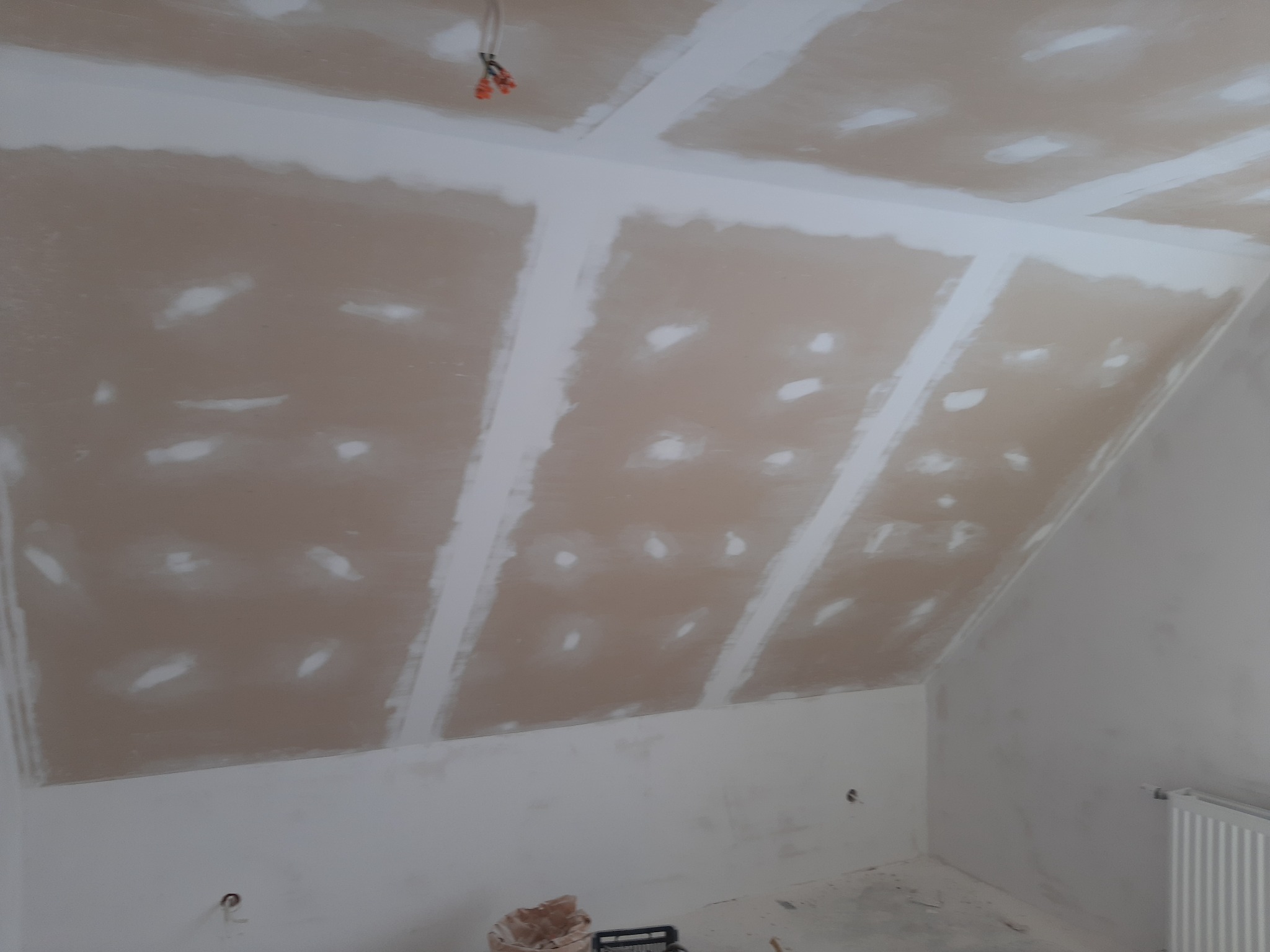 Skośny sufit poddasza z płyt kartonowo-gipsowych, widoczne łączenia płyt wypełnione masą szpachlową, przygotowane do szlifowania.