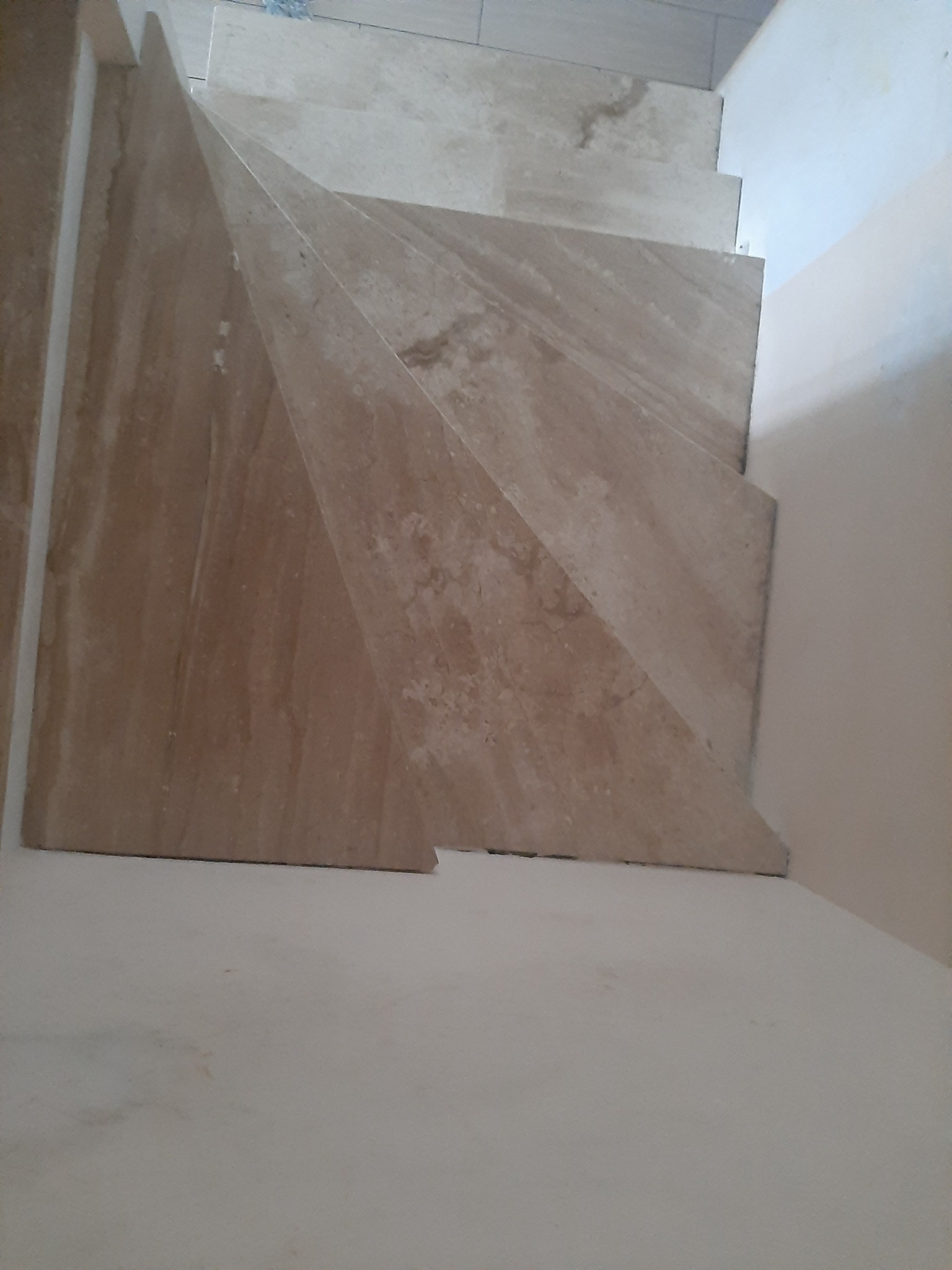 Wykończone schody wewnętrzne z płytek imitujących marmur, widok z dołu, jasne ściany.