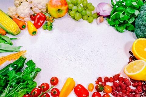 Kompozycja świeżych warzyw i owoców ułożonych w ramkę na jasnym tle, z widoczną przestrzenią w środku, idealna do prezentacji zbilansowanej diety.
