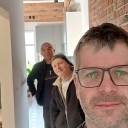 Instalacje Tomasz Magnuszewski - Trzech mężczyzn w korytarzu z drewnianymi belkami i ceglaną ścianą. Widoczne oświetlenie punktowe. Selfie jednego z nich.