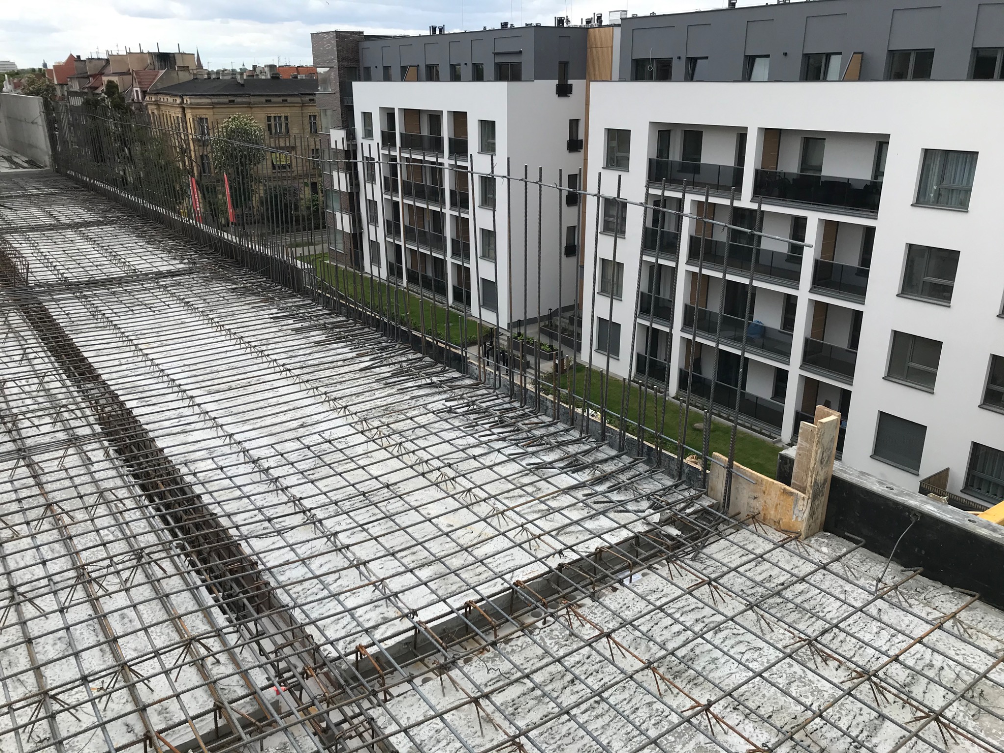 Zbrojenie stropu budynku wielorodzinnego, widok z góry na siatkę z prętów stalowych, w tle nowoczesna architektura.