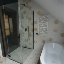 Nowoczesna łazienka na poddaszu z kabiną prysznicową typu walk-in z czarnymi profilami, heksagonalnymi płytkami z motywem kwiatowym, grzejnikiem drabinkowym i białą wanną.