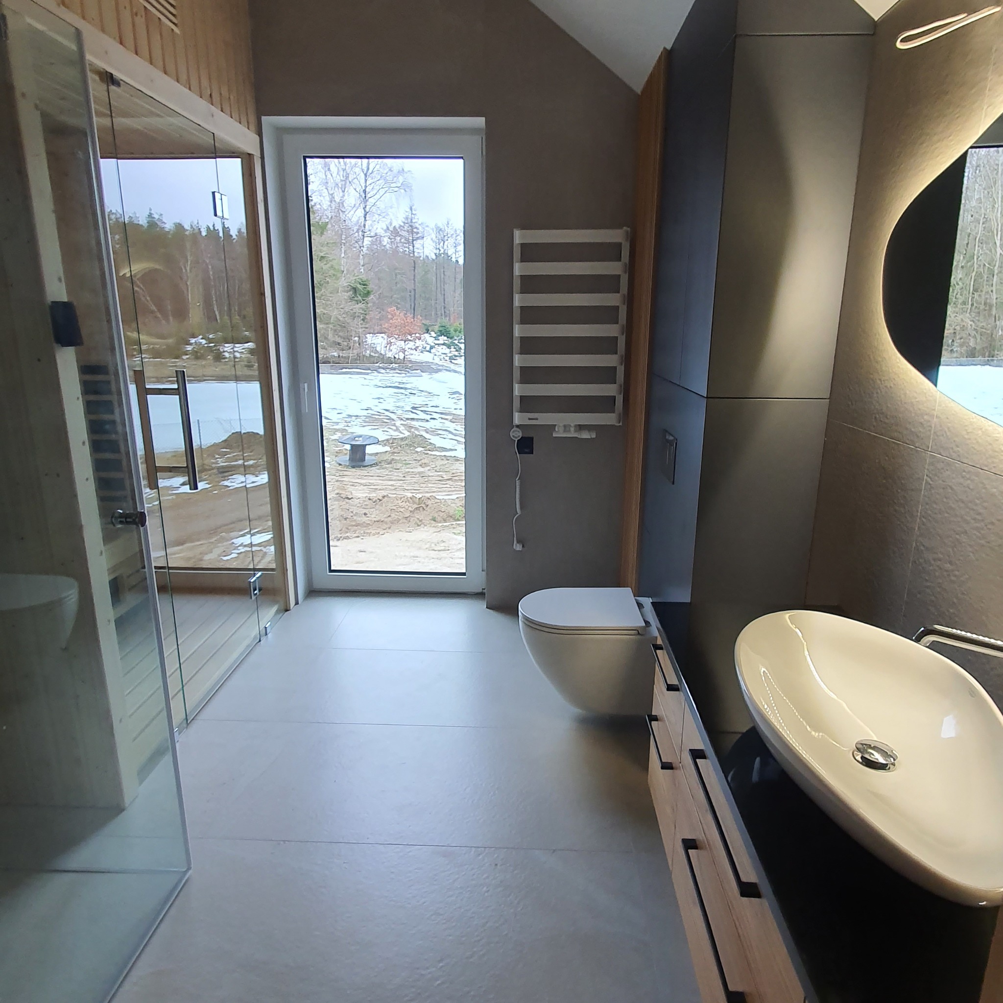 Nowoczesna łazienka z kabiną prysznicową, umywalką nablatową i widokiem na zimowy krajobraz za oknem.