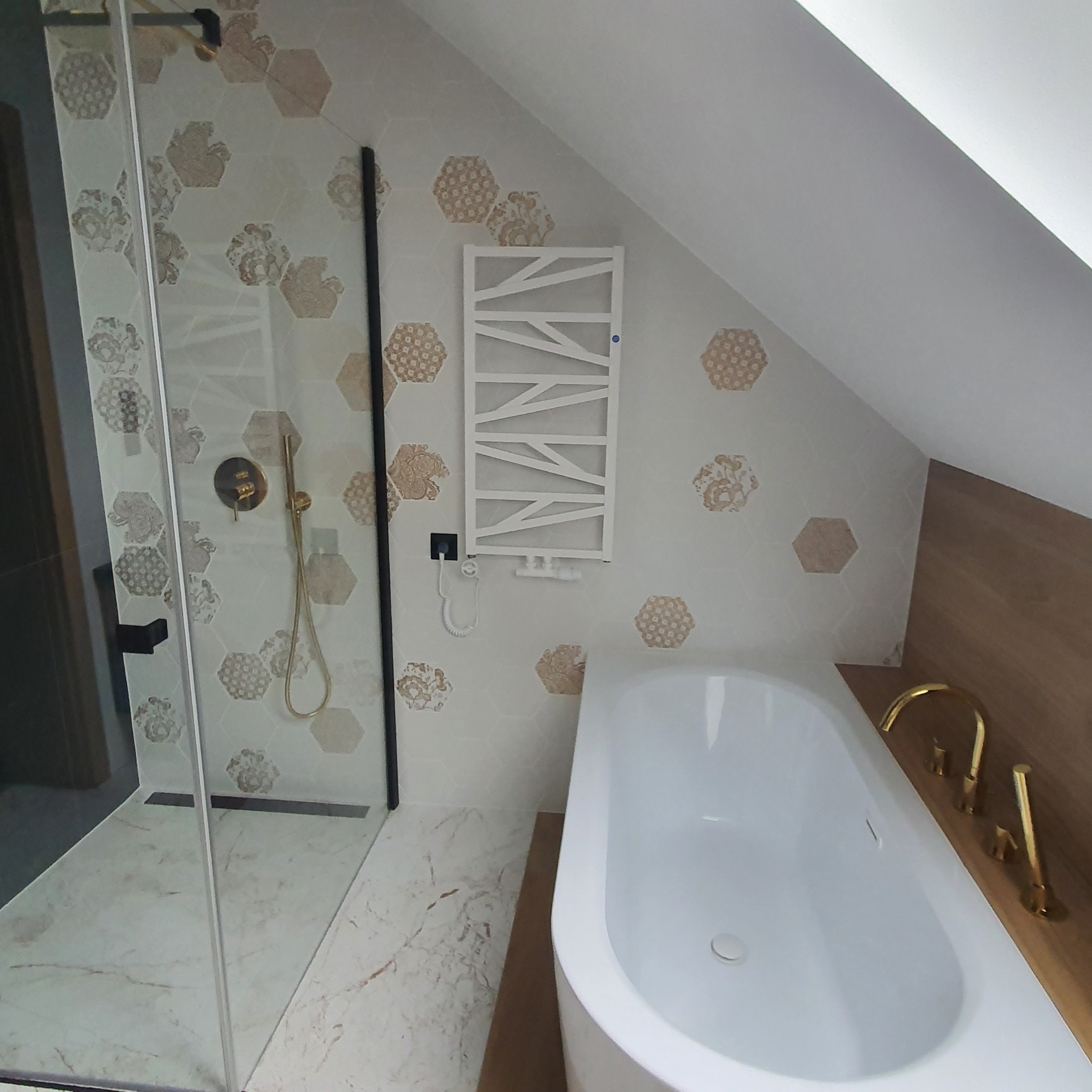 Nowoczesna łazienka na poddaszu z kabiną prysznicową typu walk-in, białą wanną, grzejnikiem drabinkowym i heksagonalnymi płytkami z motywem kwiatowym.