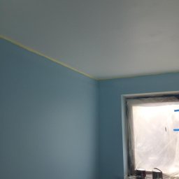 Bud-Men - Świeżo pomalowane na błękitno ściany i sufit zabezpieczone taśmą malarską, okno osłonięte folią malarską, dwie puszki z farbą na parapecie.