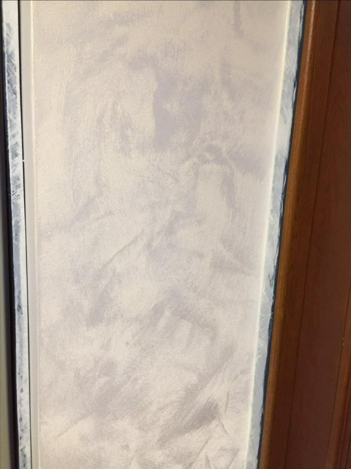 Ściana z efektem dekoracyjnym Jeger, wykończona w odcieniach szarości i bieli, z widoczną strukturą i delikatnym połyskiem, przylegająca do ramy okiennej i drewnianej futryny.