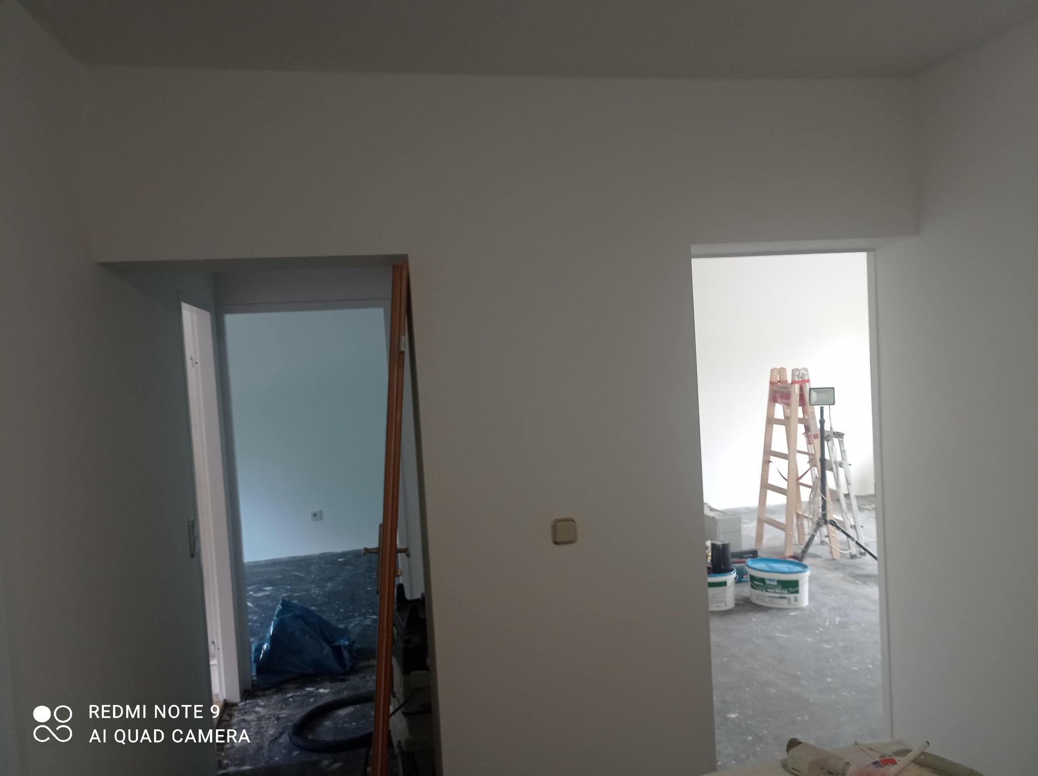 Wnętrze w trakcie odświeżania w Gorzowie Wielkopolskim, widoczne otwarte drzwi, drabina malarska, puszki z farbą i zabezpieczona folią podłoga w kolejnym pomieszczeniu.