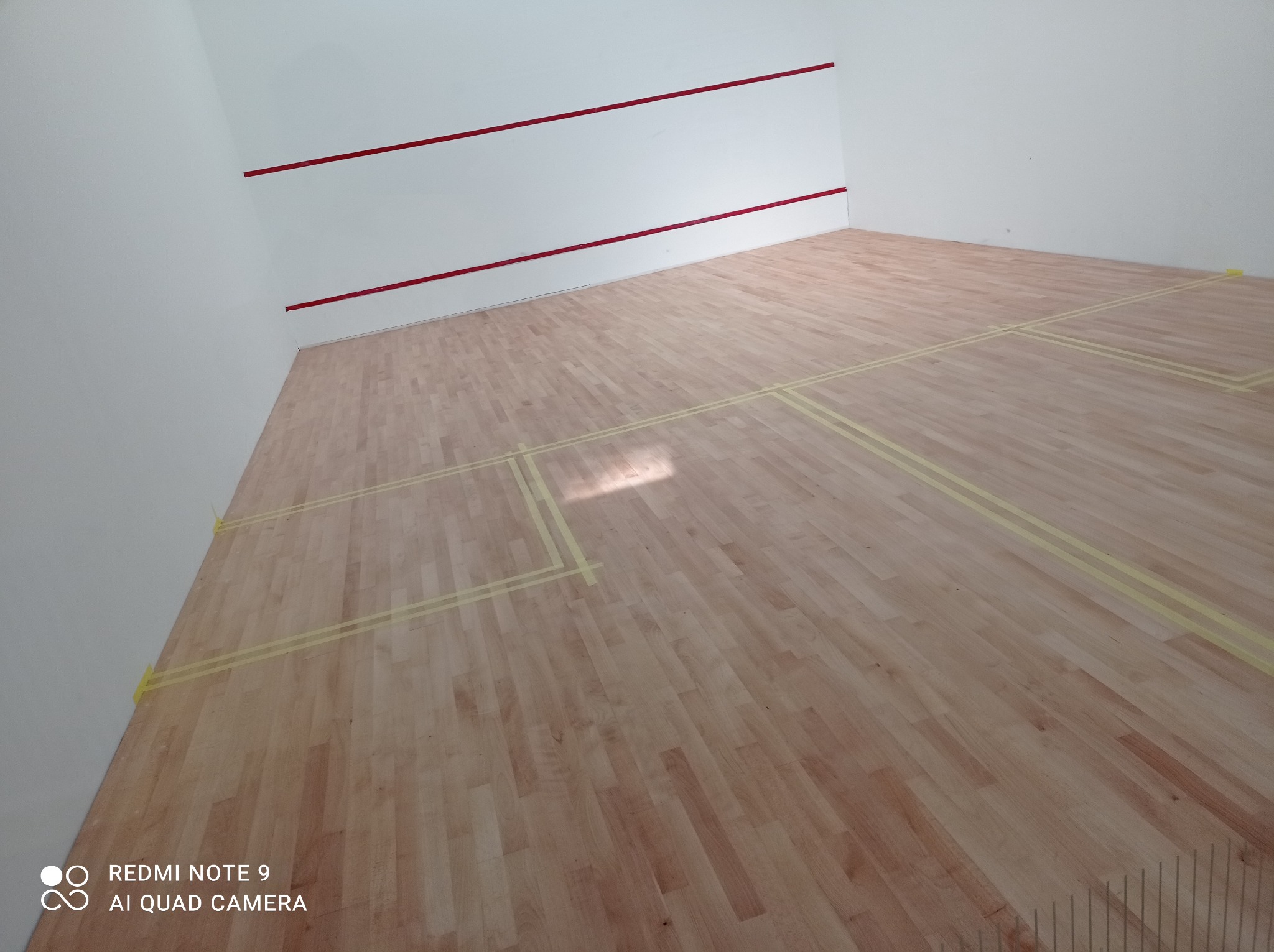 Sala do squasha z nową drewnianą podłogą parkietową, wyznaczonymi liniami na podłodze i czerwonymi liniami na białych ścianach.