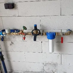 Instalacja wodna z filtrem i zaworami zamontowana na ścianie z bloczków betonowych w trakcie budowy.