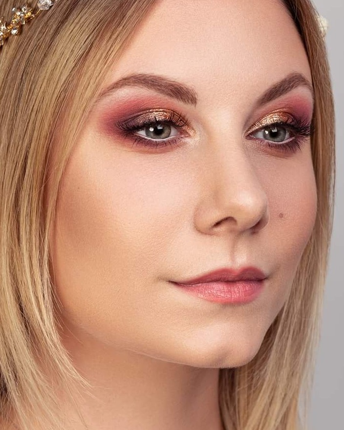 Portret kobiety z blond włosami i efektownym makijażem oczu w odcieniach różu i złota, uzupełnionym delikatną tiarą.